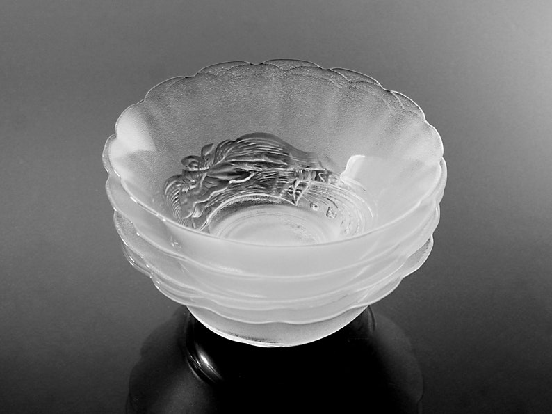 May include: A stack of frosted glass bowls with a scalloped rim. The bowls have a detailed, raised design in the center. The bowls are stacked on top of each other, creating a layered effect. The bowls are likely for serving.