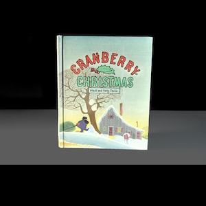 May include: A hardcover book titled "Cranberry Christmas" with a winter scene illustration. The cover features a house, a tree, and a person pulling a Christmas tree. The title is in red and green, with the authors' names below.