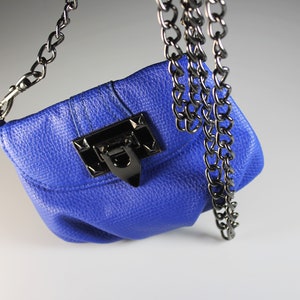 Pode incluir: Uma pequena bolsa azul cobalto com um acabamento texturizado. A bolsa apresenta um fecho de metal preto e uma al&ccedil;a de corrente a condizer. A corrente &eacute; presa &agrave;s laterais da bolsa.