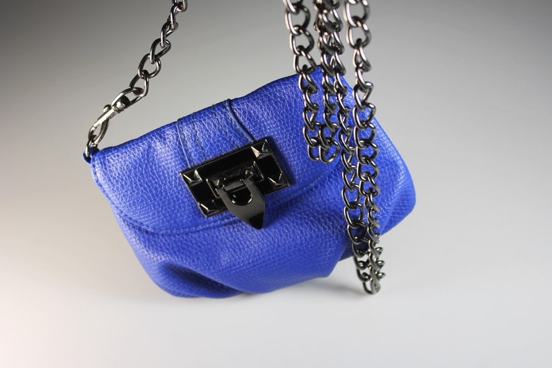 Pode incluir: Uma pequena bolsa azul cobalto com um acabamento texturizado. A bolsa apresenta um fecho de metal preto e uma al&ccedil;a de corrente a condizer. A corrente &eacute; presa &agrave;s laterais da bolsa.