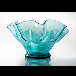 May include: A turquoise blue glass bowl with a ruffled rim and a textured surface. The bowl has a wide, shallow base and a narrow, cylindrical stem.