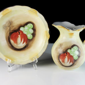 Puede incluir: Un juego vintage de vajilla de cocina de porcelana con un taz&oacute;n y una jarra de color crema con un dise&ntilde;o pintado a mano de manzanas rojas y uvas verdes.