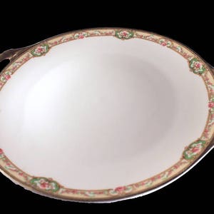 May include: A white porcelain serving dish with gold trim and a floral pattern. The dish has two handles and is oval shaped.