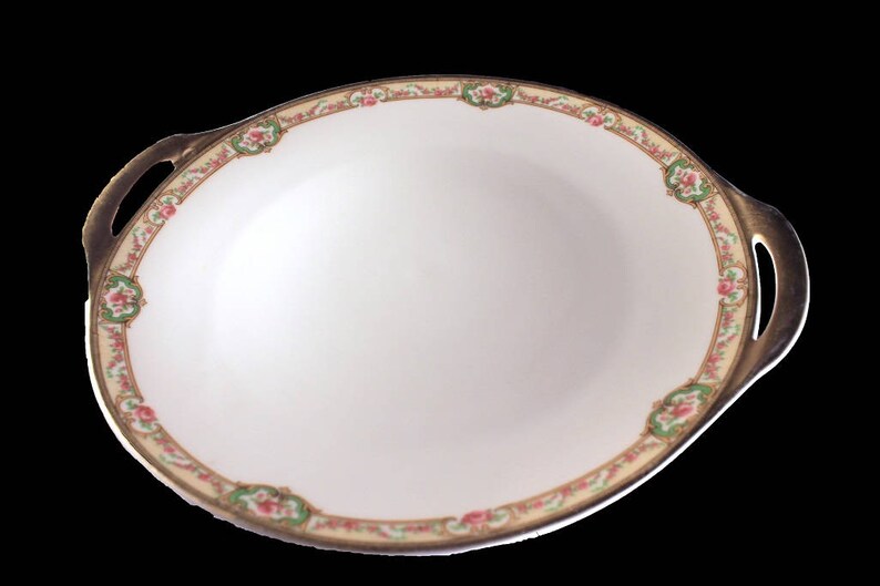 May include: A white porcelain serving dish with gold trim and a floral pattern. The dish has two handles and is oval shaped.