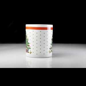 May include: White ceramic mug with a green Christmas tree design and red polka dots. The mug has a red band around the top.