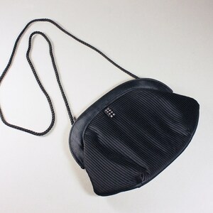 May include: A black pleated evening bag with a chain strap and a small, silver, decorative detail.