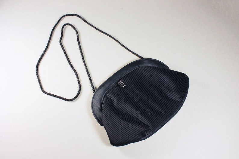 May include: A black pleated evening bag with a chain strap and a small, silver, decorative detail.
