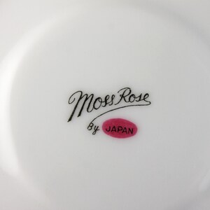 Peut inclure: Une assiette en c&eacute;ramique blanche avec une inscription cursive noire qui dit "Moss Rose" et un ovale rouge avec le mot "JAPAN" &agrave; l'int&eacute;rieur.