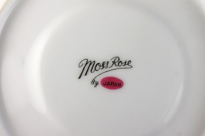 Peut inclure: Une assiette en c&eacute;ramique blanche avec une inscription cursive noire qui dit "Moss Rose" et un ovale rouge avec le mot "JAPAN" &agrave; l'int&eacute;rieur.
