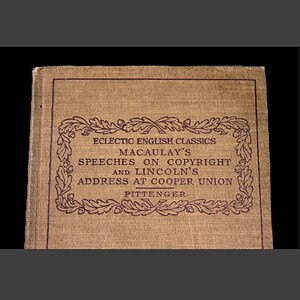 Op de afbeelding: Een bruin boek met een bordeauxrode rand en tekst die luidt "Eclectic English Classics Macaulay's Speeches on Copyright and Lincoln's Address at Cooper Union Pittenger".