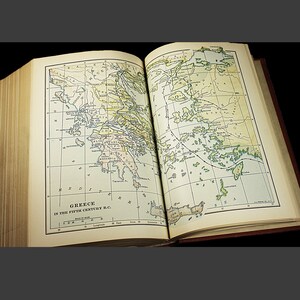 May include: An open book displaying a map of Greece in the 5th Century B.C. The map is coloured and shows the different regions of Greece, including Athens, Sparta, and Thebes. The map is surrounded by a grid of lines, which are labelled with numbers and letters.