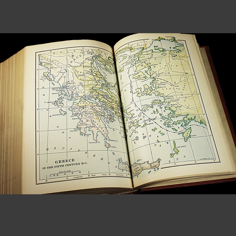 May include: An open book displaying a map of Greece in the 5th Century B.C. The map is coloured and shows the different regions of Greece, including Athens, Sparta, and Thebes. The map is surrounded by a grid of lines, which are labelled with numbers and letters.