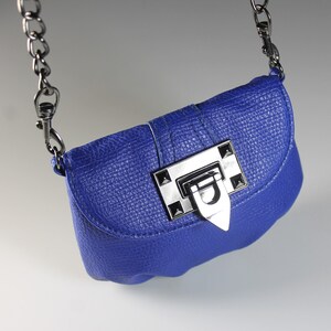 Pode incluir: Uma bolsa transversal azul cobalto com acabamento texturizado. A bolsa apresenta um fecho de metal prateado e uma al&ccedil;a de corrente. A bolsa tem formato retangular pequeno.