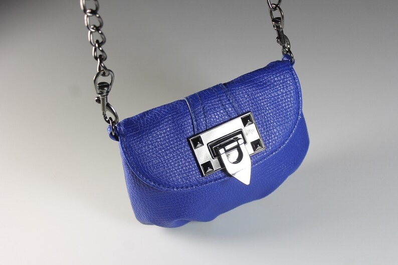 Pode incluir: Uma bolsa transversal azul cobalto com acabamento texturizado. A bolsa apresenta um fecho de metal prateado e uma al&ccedil;a de corrente. A bolsa tem formato retangular pequeno.