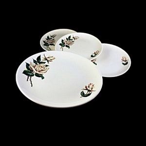 May include: Set of four white ceramic plates with a floral design featuring white roses with green leaves.