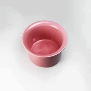 May include: A pink ceramic bowl with a smooth, rounded interior. The bowl is empty and has a slightly flared rim.