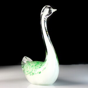 May include: A white glass swan figurine with green speckled accents. The swan has a long, curved neck and a small head.