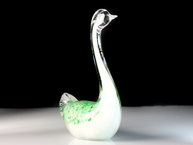 May include: A white glass swan figurine with green speckled accents. The swan has a long, curved neck and a small head.