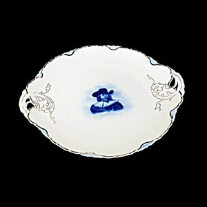 May include: A white porcelain serving platter with a blue and white image of a man in a hat. The platter has gold trim and two ornate handles.