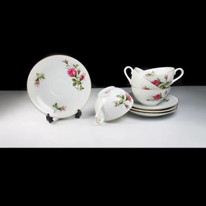 Peut inclure: Ensemble de quatre tasses &agrave; th&eacute; et soucoupes en porcelaine blanche avec un motif floral repr&eacute;sentant des roses roses. Les tasses ont des anses et les soucoupes ont un bord dor&eacute;.