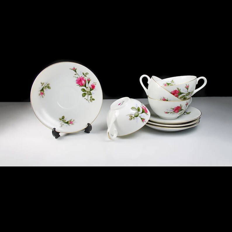 Peut inclure: Ensemble de quatre tasses &agrave; th&eacute; et soucoupes en porcelaine blanche avec un motif floral repr&eacute;sentant des roses roses. Les tasses ont des anses et les soucoupes ont un bord dor&eacute;.