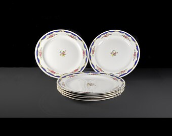May include: A set of white porcelain plates with a blue floral border and a small floral design in the center. The plates are stacked and arranged on a dark surface. The plates are a classic design.