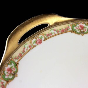 May include: A white porcelain serving dish with a gold rim and floral design. The dish has a scalloped edge and a handle on one side.