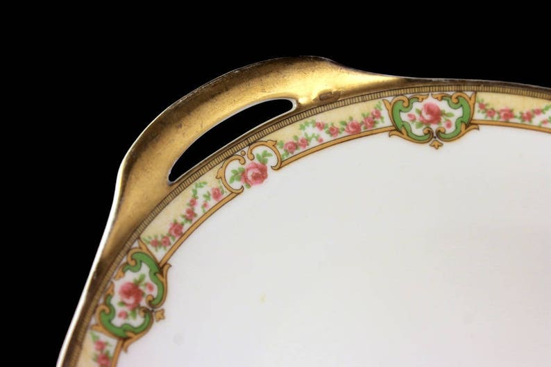 May include: A white porcelain serving dish with a gold rim and floral design. The dish has a scalloped edge and a handle on one side.