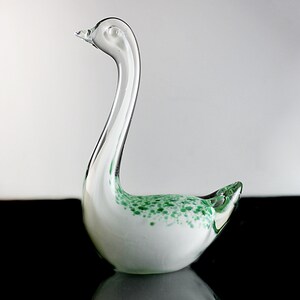 May include: A white glass swan figurine with green flecks throughout. The swan has a long neck and a small head.
