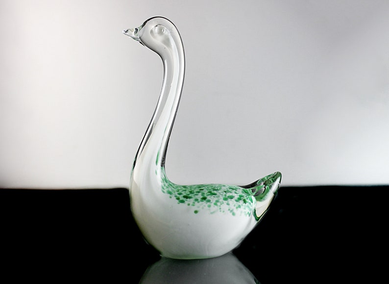 May include: A white glass swan figurine with green flecks throughout. The swan has a long neck and a small head.
