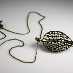 May include: A delicate gold-toned necklace with a leaf-shaped pendant. The pendant is made of intricate metalwork and has a delicate, openwork design.