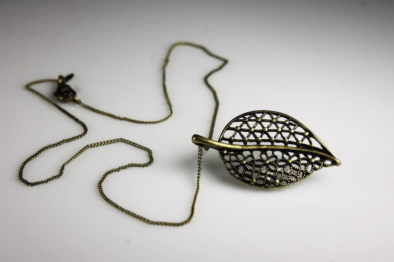 May include: A delicate gold-toned necklace with a leaf-shaped pendant. The pendant is made of intricate metalwork and has a delicate, openwork design.