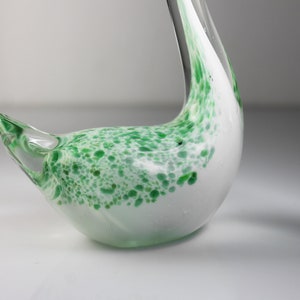 May include: A white glass swan figurine with green speckled accents. The swan has a long neck and a curved body.