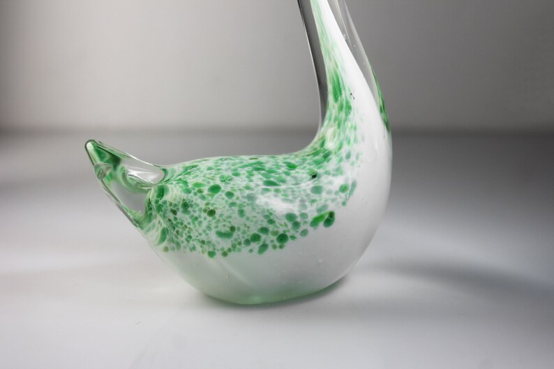 May include: A white glass swan figurine with green speckled accents. The swan has a long neck and a curved body.