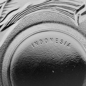 May include: Close-up of a clear glass bowl with embossed floral and leaf designs. The word "INDONESIA" is embossed on the bottom of the bowl. The bowl has a textured surface.