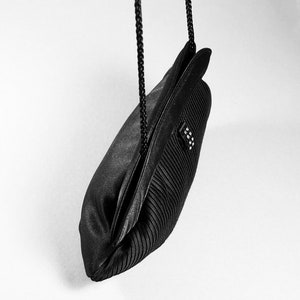 May include: A black satin evening bag with a pleated design and a black chain strap.