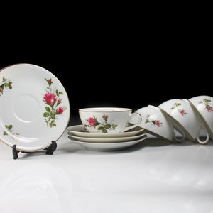 Peut inclure: Ensemble de quatre tasses &agrave; th&eacute; et soucoupes blanches avec un motif floral repr&eacute;sentant des roses roses et des feuilles vertes. Les tasses et les soucoupes ont un bord dor&eacute;.