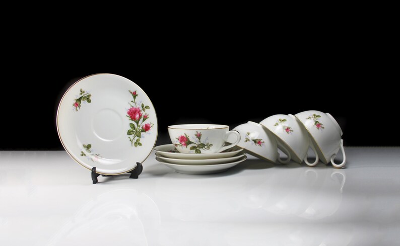 Peut inclure: Ensemble de quatre tasses &agrave; th&eacute; et soucoupes blanches avec un motif floral repr&eacute;sentant des roses roses et des feuilles vertes. Les tasses et les soucoupes ont un bord dor&eacute;.