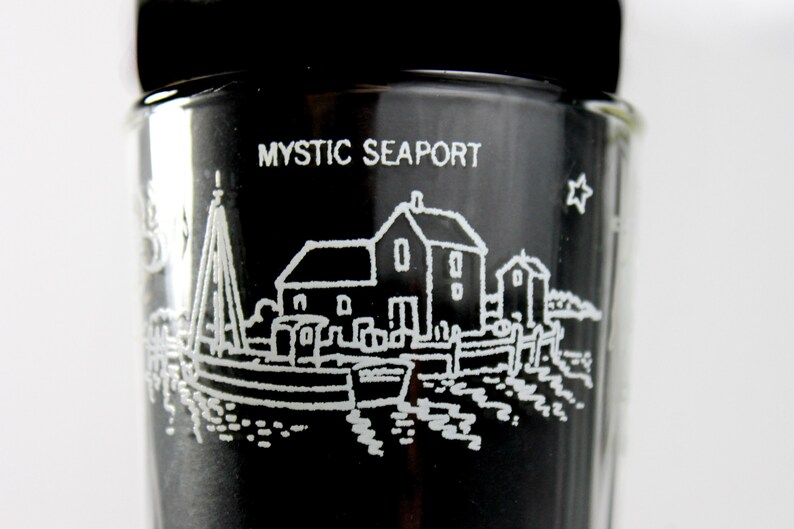 以下が含まれることがあります： 側面に「MYSTIC SEAPORT」の文字が書かれた、小さな町が白く描かれた黒いガラス