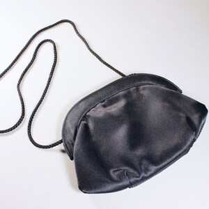 May include: A black satin clutch bag with a long black braided strap.