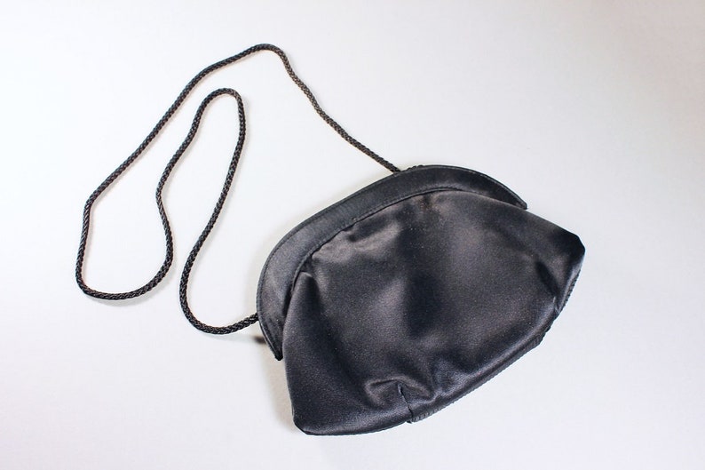 May include: A black satin clutch bag with a long black braided strap.