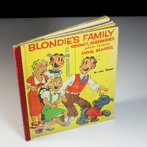 May include: A yellow book cover with the title "Blondie's Family Cookie, Alexander and Their Dog, Elmer" by Chic Young. The cover features a cartoon illustration of Blondie, Dagwood, Alexander, and Elmer.