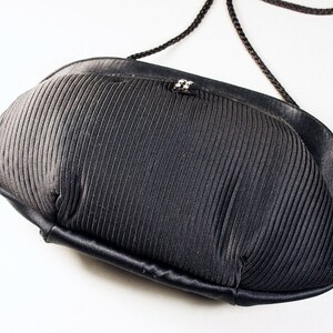May include: A black, pleated, fabric evening bag with a black cord strap.