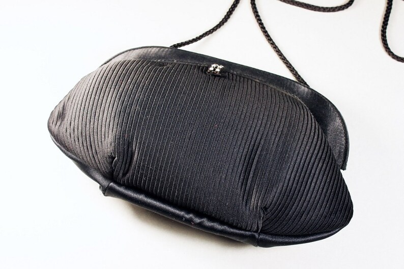 May include: A black, pleated, fabric evening bag with a black cord strap.