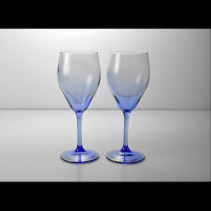 Puede incluir: Dos copas de vino con cuencos transparentes y tallos y bases azules. Las copas están vacías y sobre una superficie blanca. El azul contrasta con el cristal transparente.