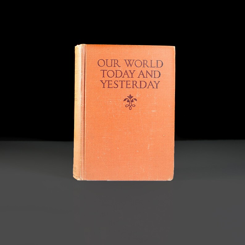 May include: A vintage orange book with the title "Our World Today and Yesterday" printed in black lettering. A small decorative design is centred below the title.