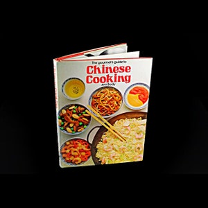 May include: A white cookbook with a red title that reads "The gourmet's guide to Chinese Cooking" by Ann Body. The cover features a variety of Chinese dishes, including stir-fried noodles, shrimp fried rice, and a side dish of peas and almonds.