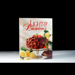 May include: A cookbook titled "Light & Luscious" with a photo of a chocolate cake with raspberries on top on the cover.