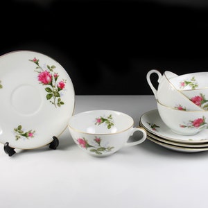 Peut inclure: Un ensemble de tasses &agrave; th&eacute; et de soucoupes blanches avec un motif floral de roses roses. Les tasses ont deux poign&eacute;es et les soucoupes ont une bordure dor&eacute;e.