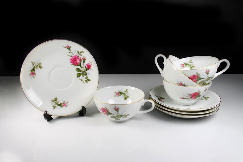 Peut inclure: Un ensemble de tasses &agrave; th&eacute; et de soucoupes blanches avec un motif floral de roses roses. Les tasses ont deux poign&eacute;es et les soucoupes ont une bordure dor&eacute;e.